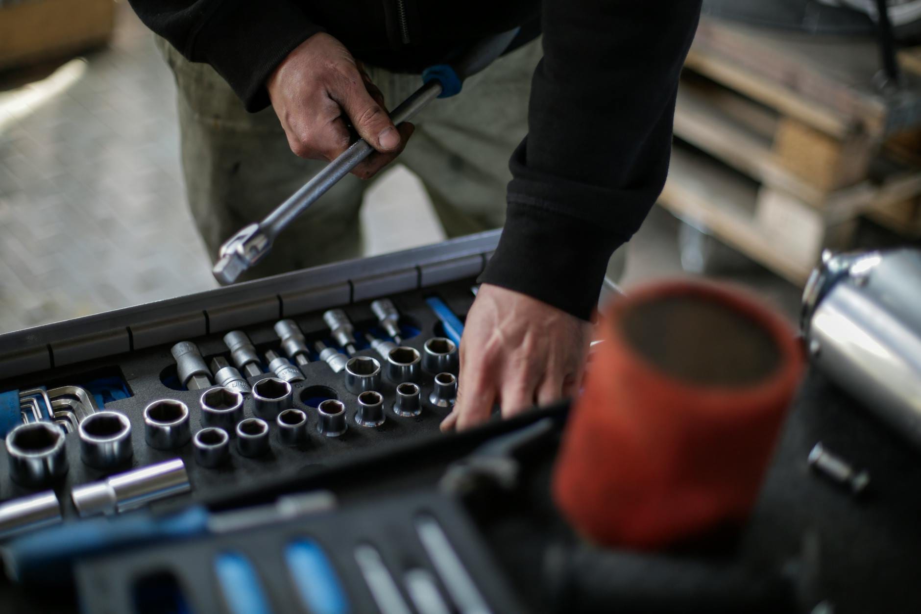 From above view of crop unrecognizable mechanic in workwear choosing metal sockets for ratchet while repairing vehicle in modern workshop